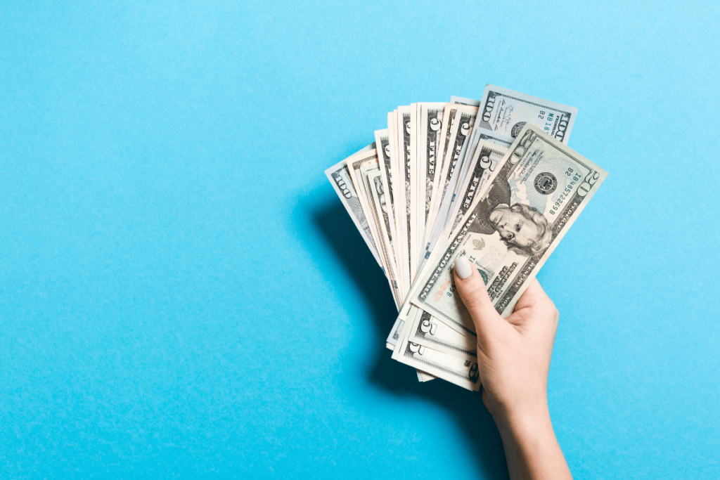 A hand holding cash against a bright blue background.