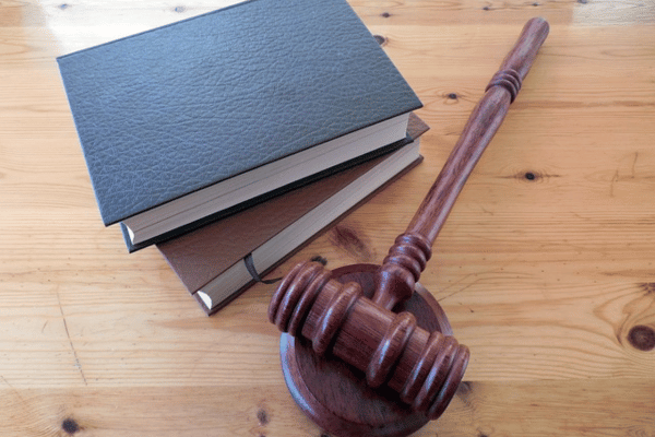 A wooden judge's gavel beside a stack of books on a wooden table, symbolizing law and regulations.